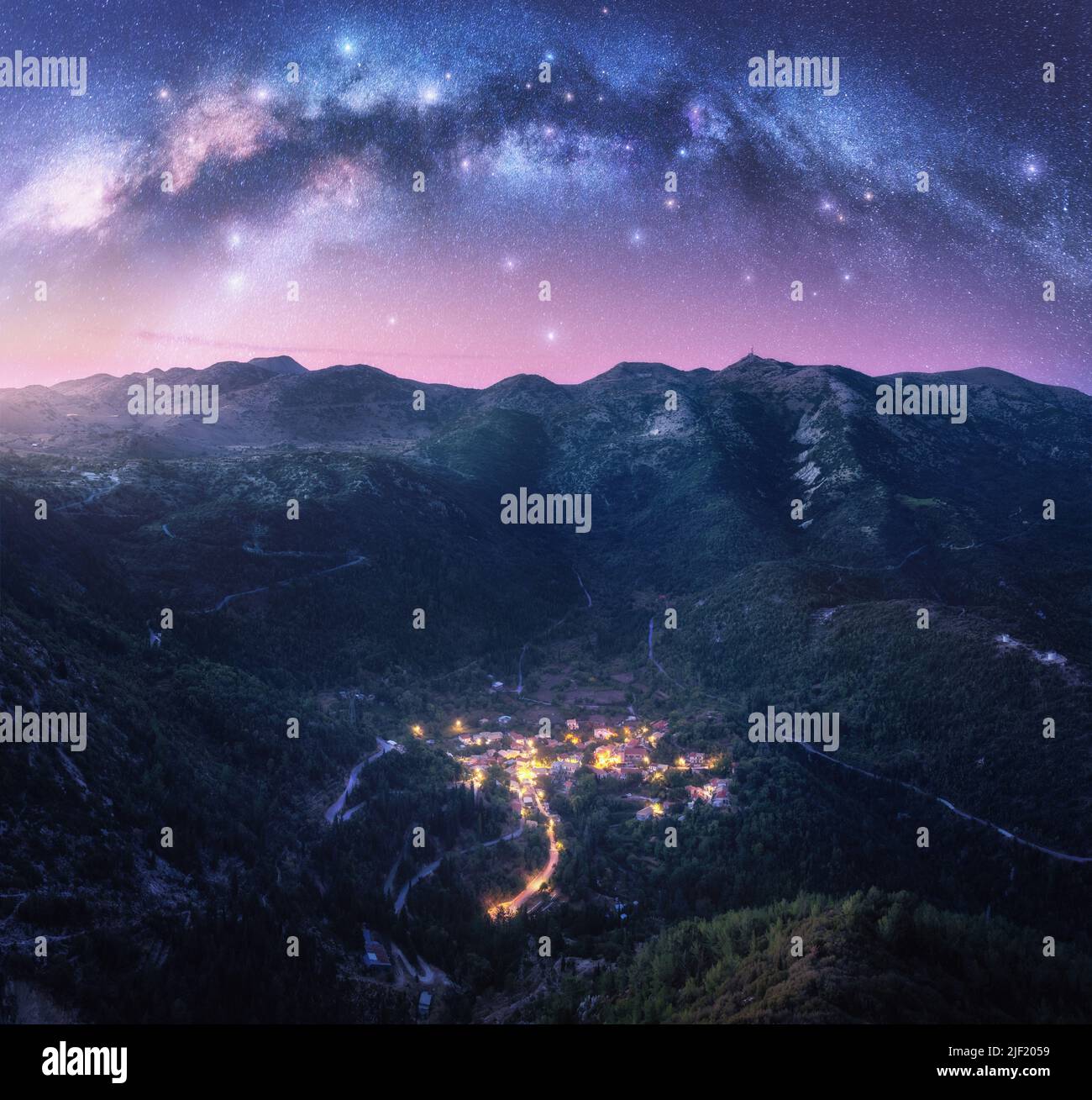 Milky Way arch and village on the mountain at night in summer Stock Photo