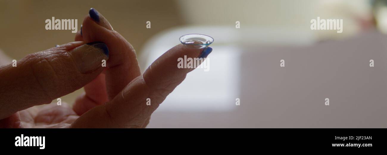 Image of a woman's hand holding a contact lens on her finger. Horizontal banner Stock Photo