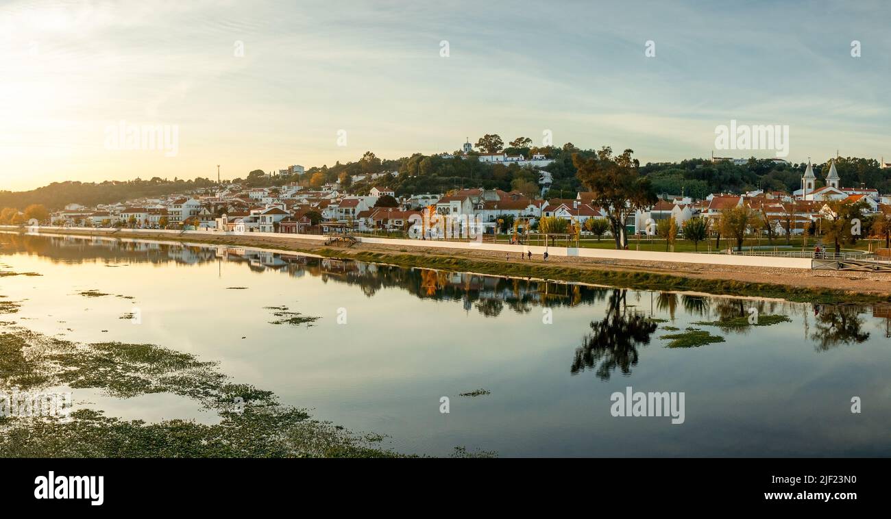 Panoramic view of the village of Coruche in Portugal at sunset, with the river Sorraia in the foreground and the riverside houses reflected. Stock Photo