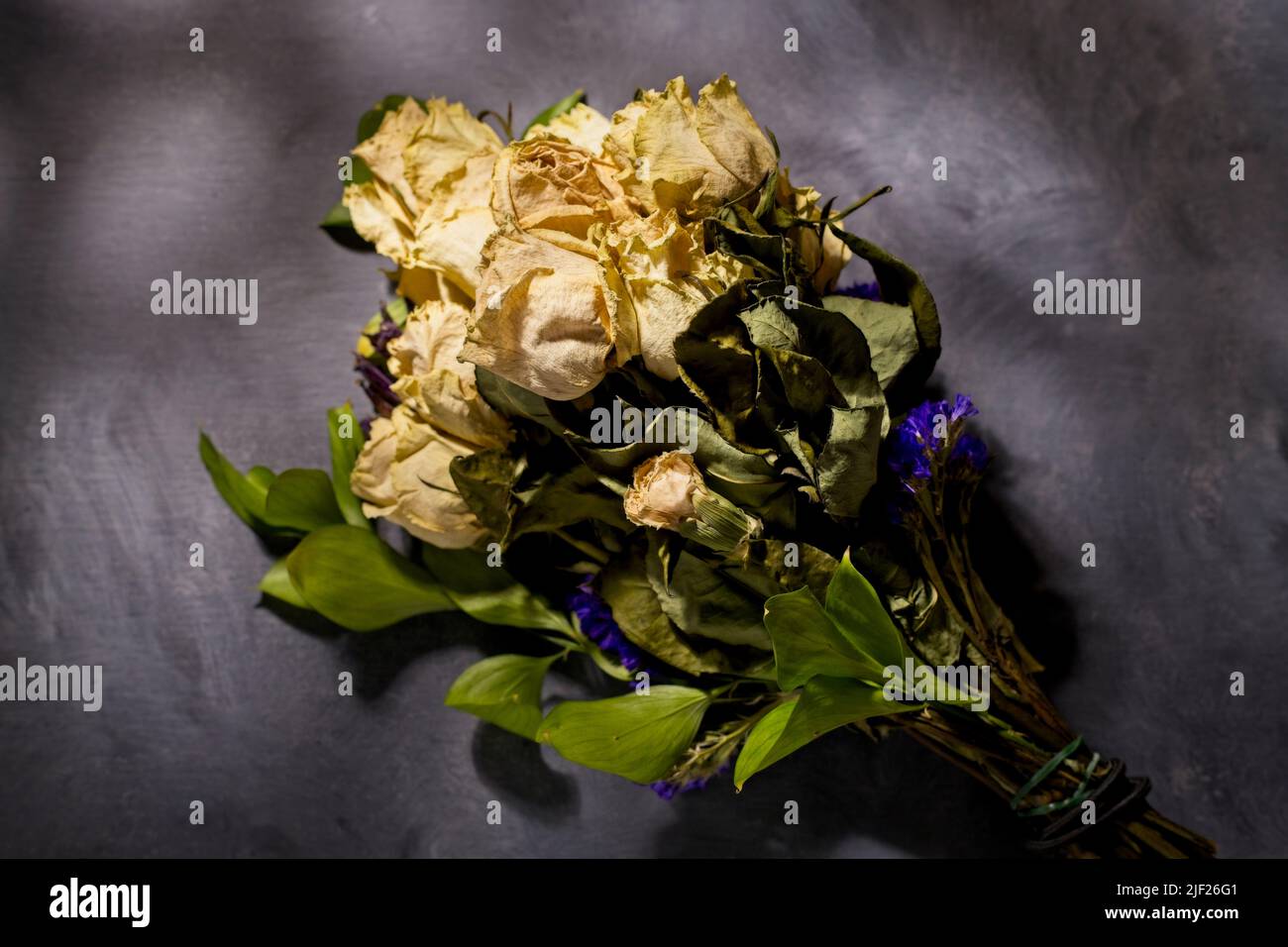 A dappled light studio photo of a bouquet of dried yellow roses on a table. Stock Photo