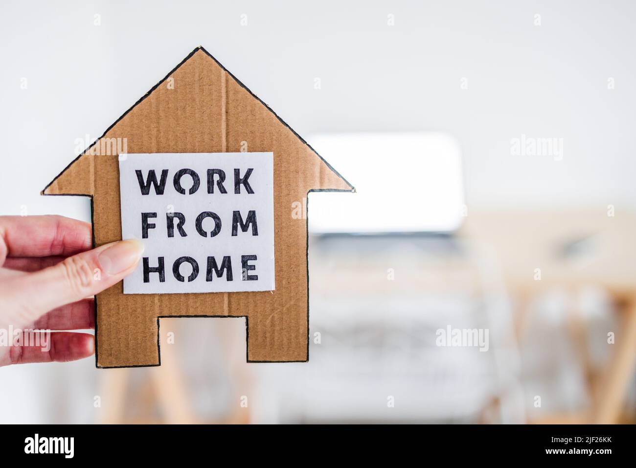 work from home sign being hold in front of out of focus home office desk setup, concept of