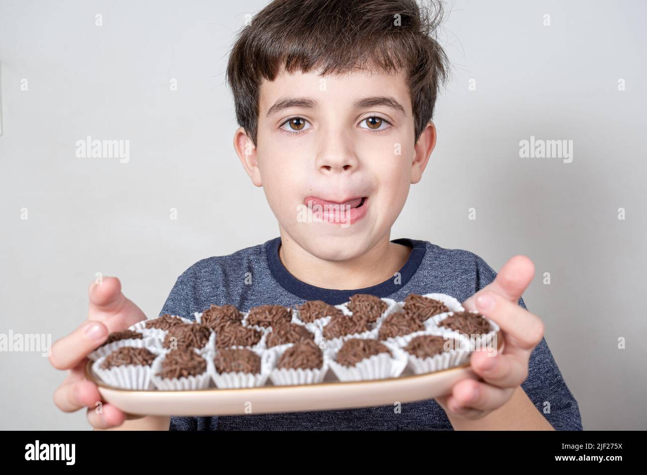 9 year old Brazilian holding a tray with several Brazilian fudge balls and licking his lips. Stock Photo