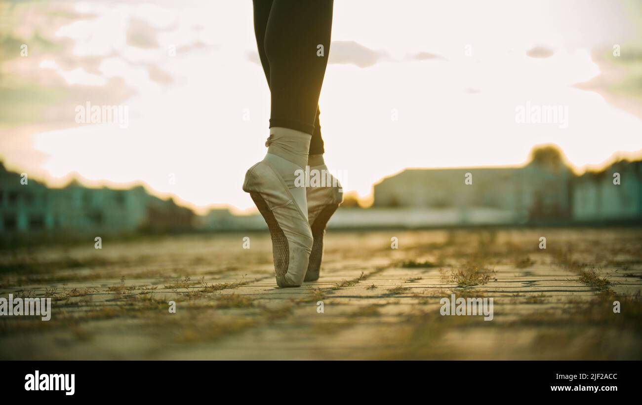 Feet of young woman ballerina standing on the roof on her tiptoes - sunset Stock Photo