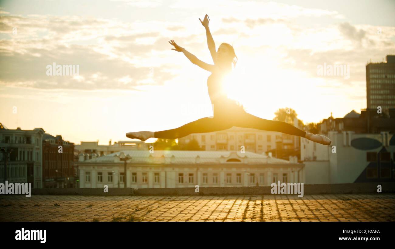 Young woman ballerina jump performing a split on a background of a beautiful bright sunset Stock Photo