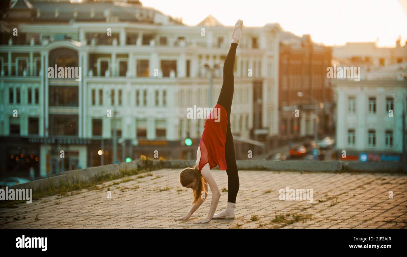 Young woman ballerina training on the roof - standing in the pose showing her stretching - touching the ground with her hands Stock Photo