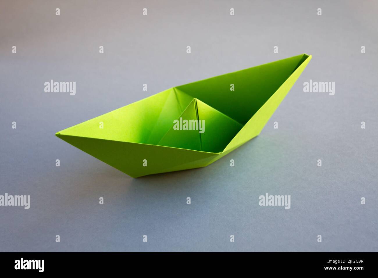 Green paper boat origami isolated on a blank grey background. Stock Photo