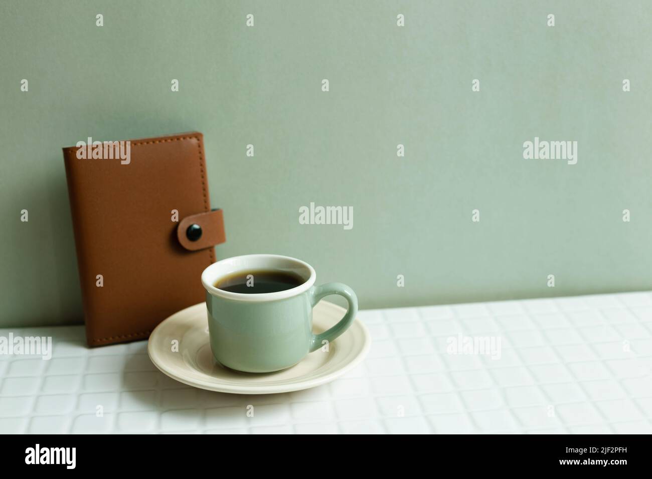Cup of coffee and diary notebook on white desk. khaki green wall background Stock Photo