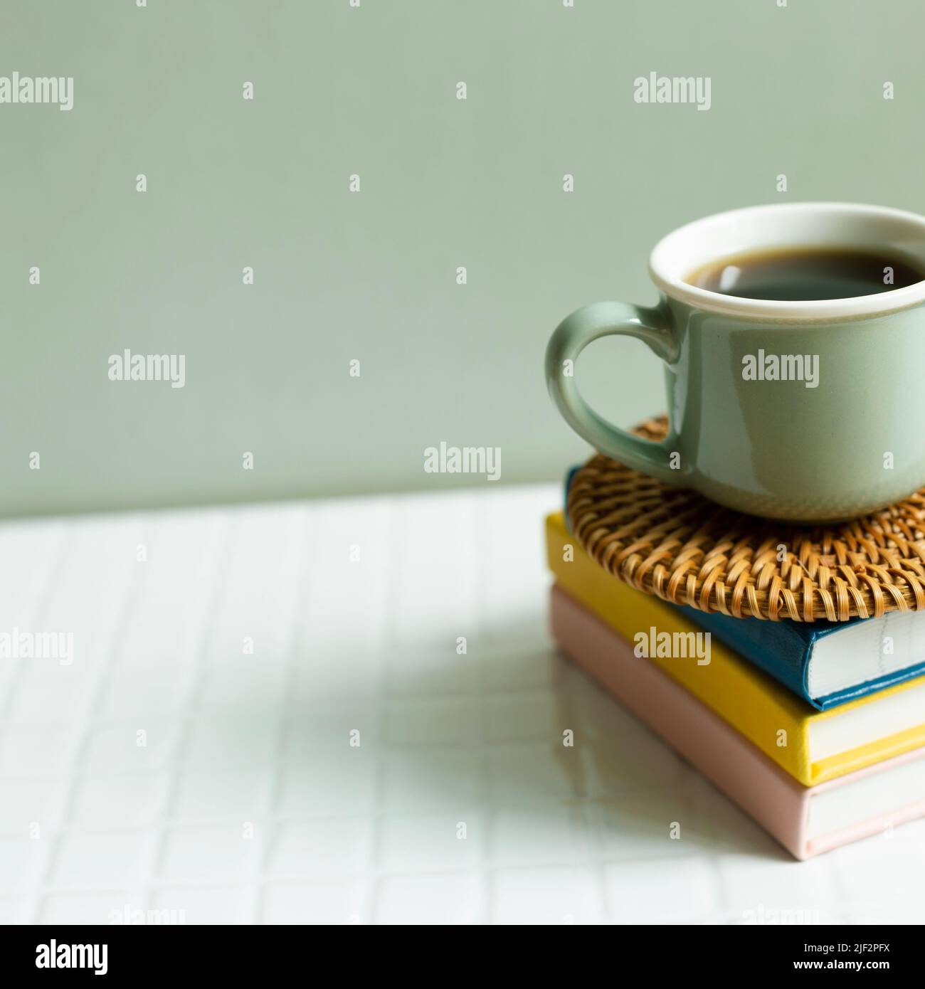 Cup of coffee and notebook on white desk. khaki green wall background Stock Photo