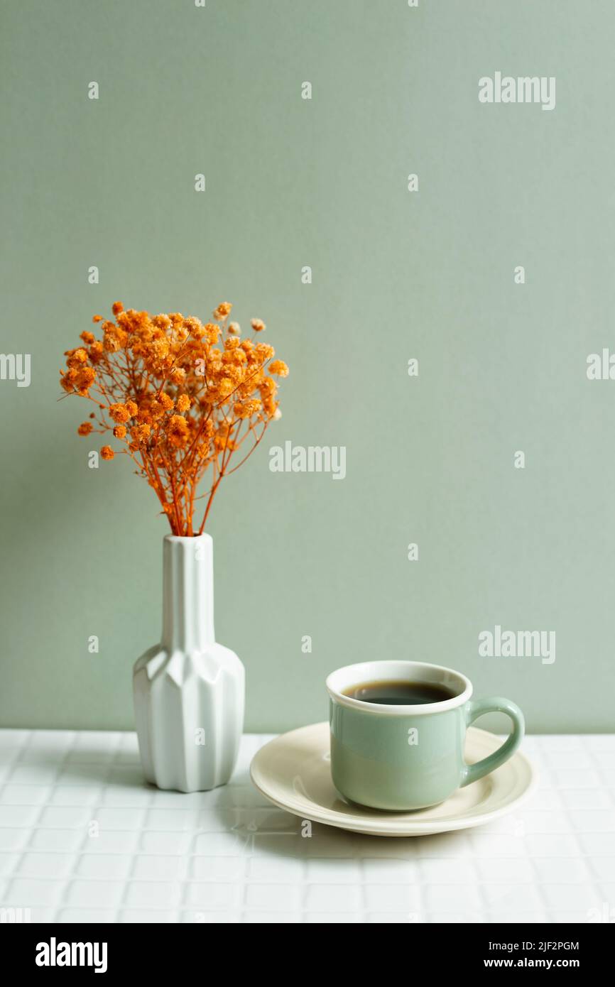Cup of coffee and orange dry flowers on white table. khaki green wall background Stock Photo