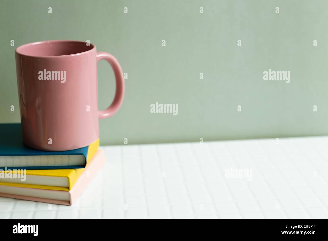 Pink cup and notebook on white desk. khaki green wall background Stock Photo