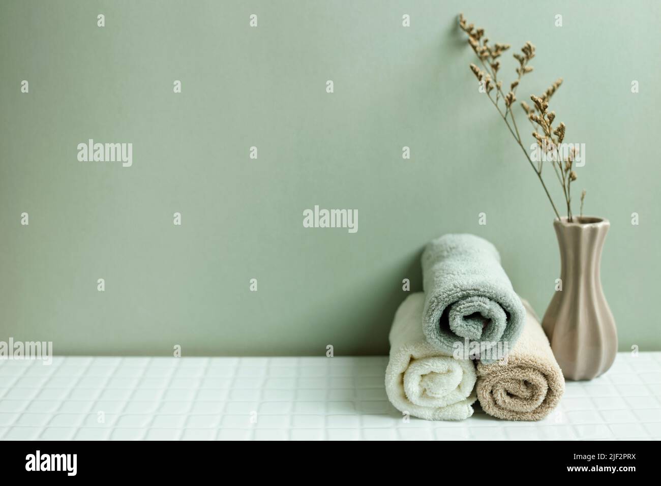 Bathroom towel and dry flower on white table. khaki green wall background. skin care and spa concept Stock Photo