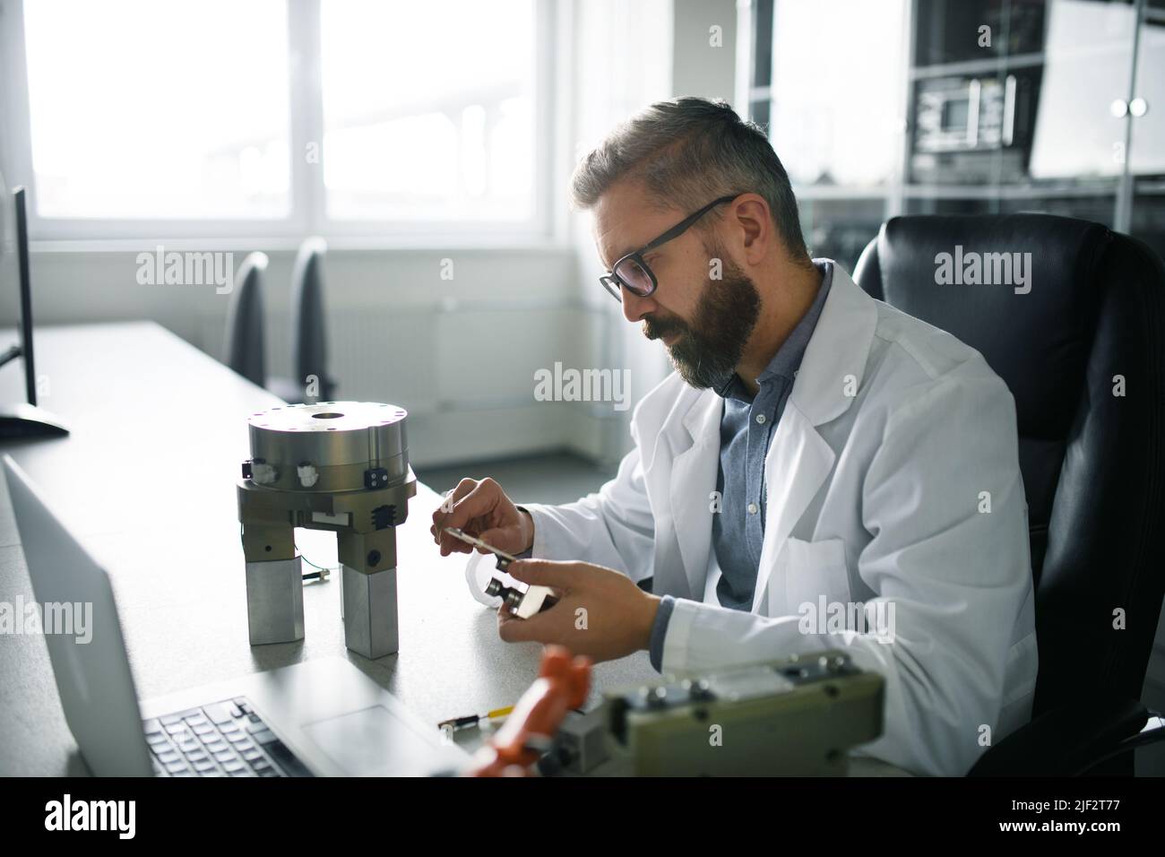 Robotics engineer working on desing of modern robotic arm adn sitting at desk in laboratory. Stock Photo