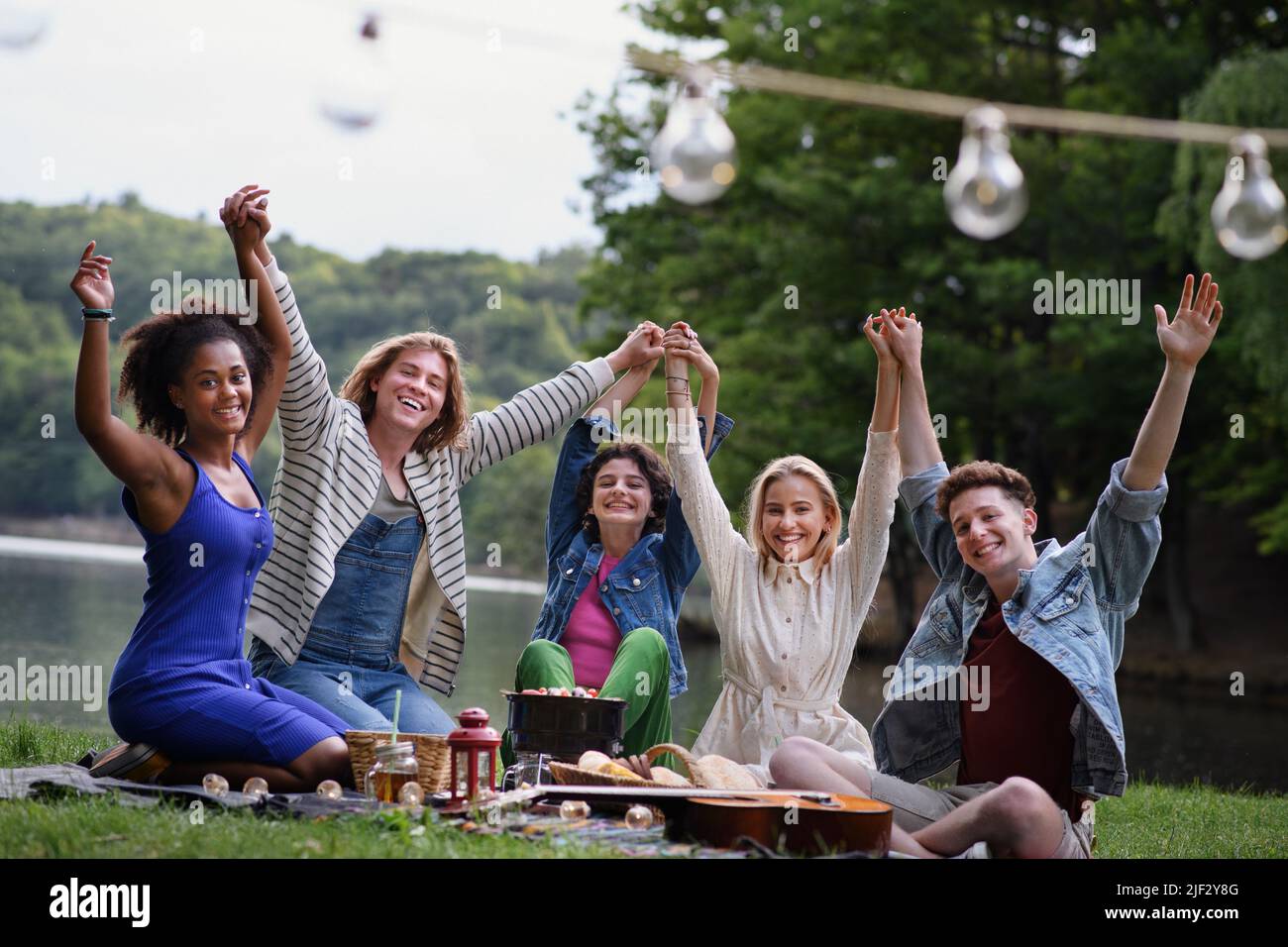 Group of young friends having fun on picnic near a lake, sitting on ...