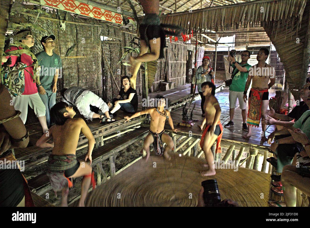Tourism workers wearing indigenous attires are tumbling on a round trampoline made of rattan at Mari Mari Cultural Village, a village that is designed to showcase the cultures of five ethnic groups of Sabah—a Malaysian state in North Borneo, which is located on the outskirts of Kota Kinabalu in Sabah, Malaysia. Stock Photo