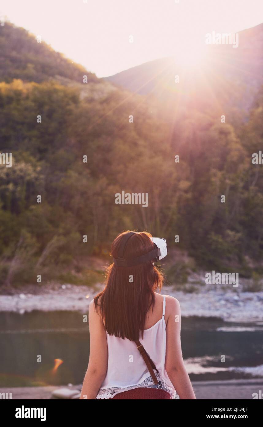 Woman using AR goggles to look at the view of the mountains. Woman on vacation wearing AR googles on holiday in the mountains. Woman playing with AR Stock Photo