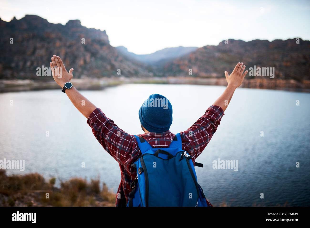 An unidentified man raises his arms at lake view while backpacking mountains Stock Photo