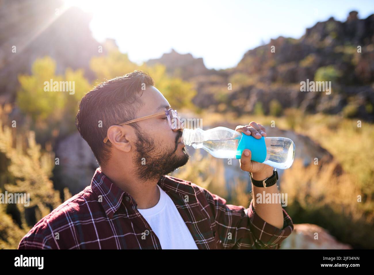 A man drinks water from a glass bottle in the sunshine on a hiking adventure Stock Photo