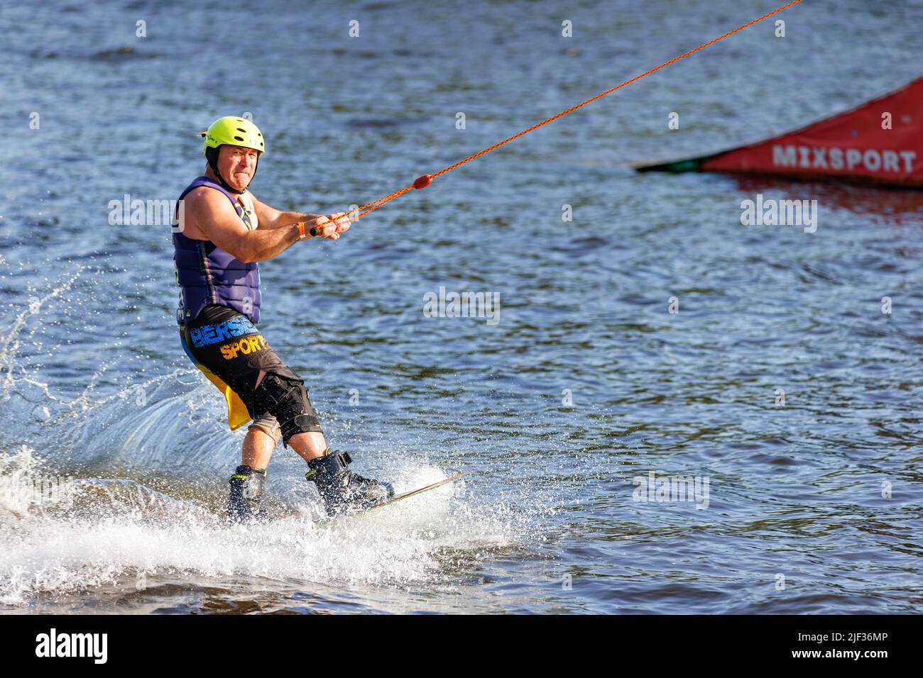 A senior wakeboarder athlete in a protective helmet and vest rides a water board in a summer river bay on a summer day. 06.19.1922. Kyiv. Ukraine. Stock Photo