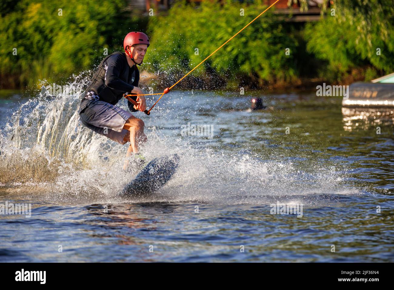 An athlete wakeboarder in a red protective helmet and a black vest raises water spray from a fast ride on a water board. 06.19.1922. Kyiv. Ukraine. Stock Photo