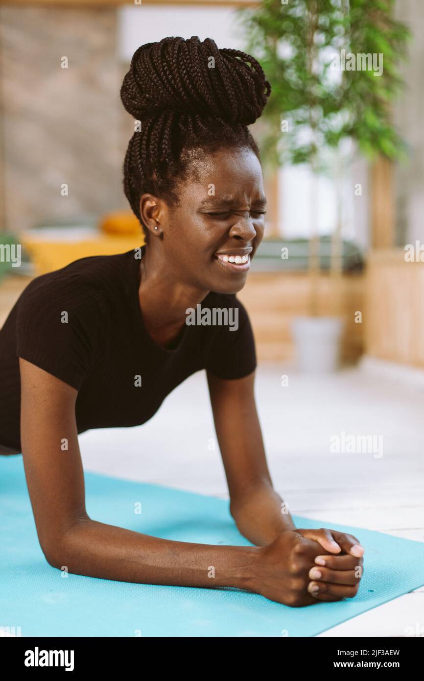 Enduring and holding on fit afro american woman standing in elbow plank closeup, training on gymnastic mat in decorated studio. Muscle strengthening Stock Photo