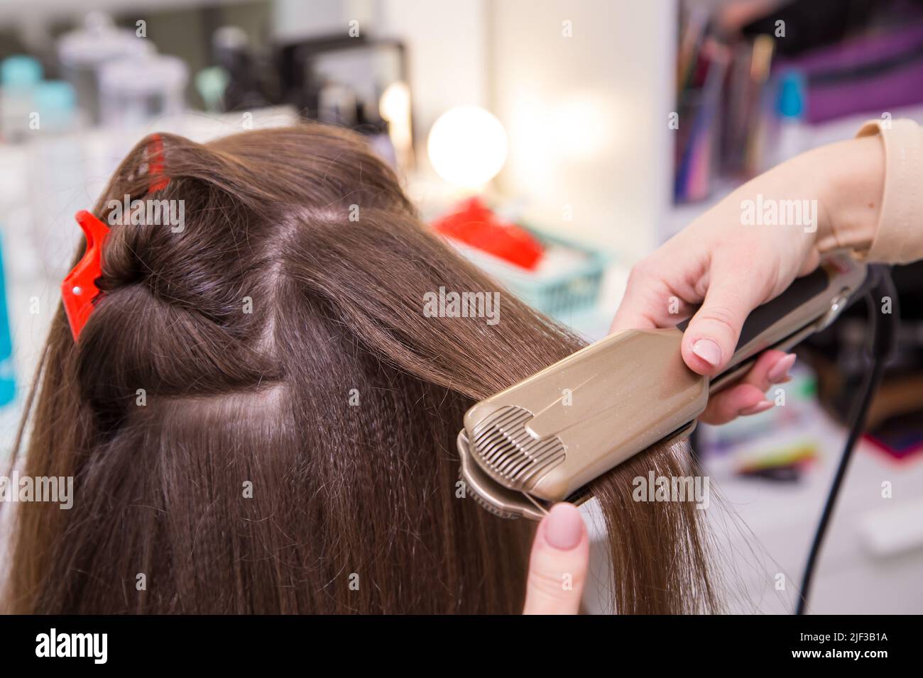 Close-up of a woman's hand straightens a lock of hair with a curling iron. The hairdresser makes a hairstyle for a young woman. Barber shop, business concept. Beauty salon, hair care. Stock Photo