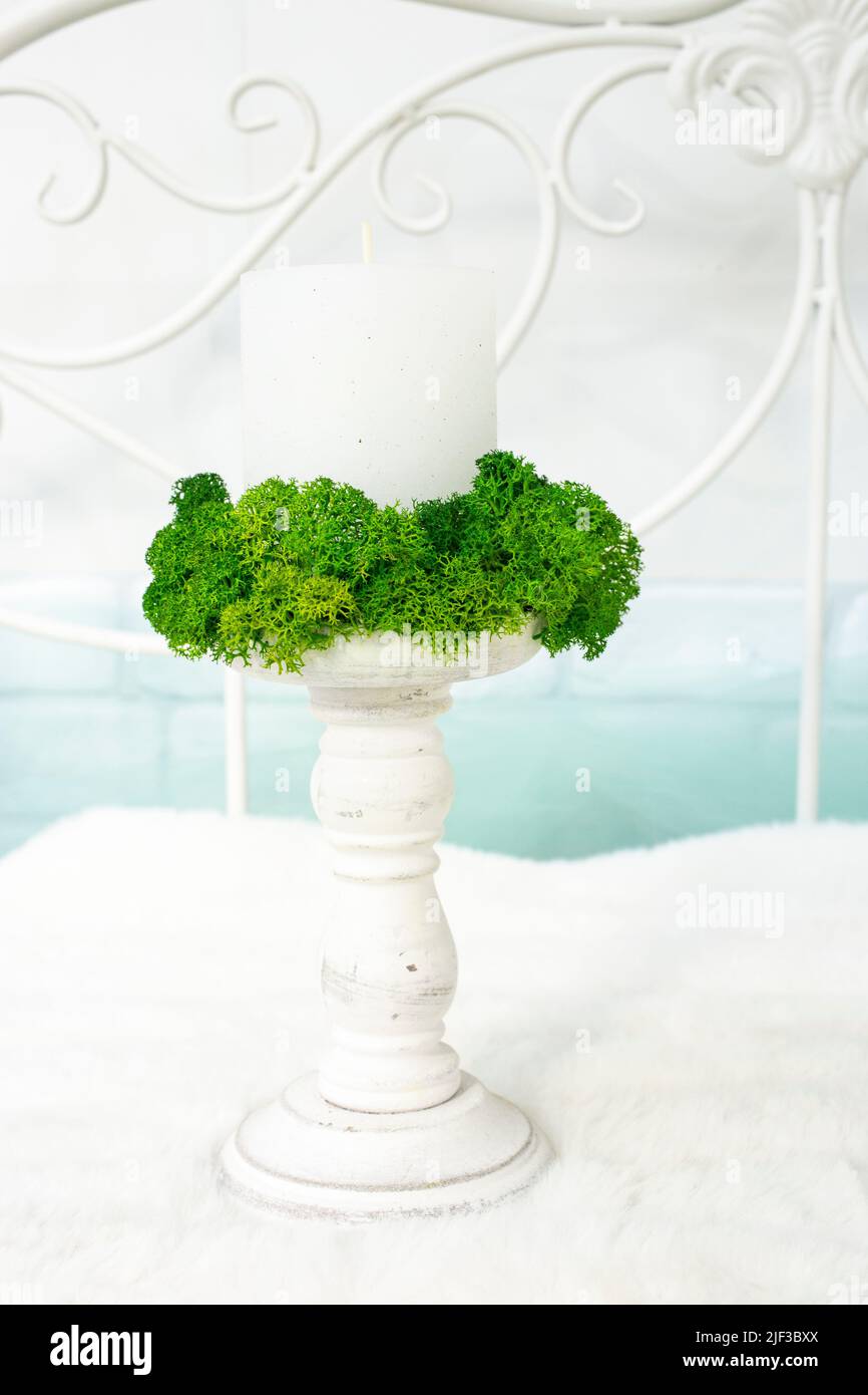 Wood candle holder with a white candle surrounded by moss, on white and
