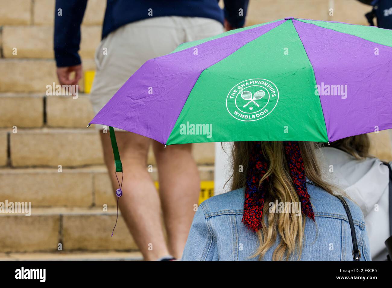 London, UK. 29th June, 2022. Tennis: Grand Slam/WTA Tour/ATP Tour - Wimbledon. A visitor carries an umbrella with the tournament logo printed on it. Credit: Frank Molter/dpa/Alamy Live News Stock Photo