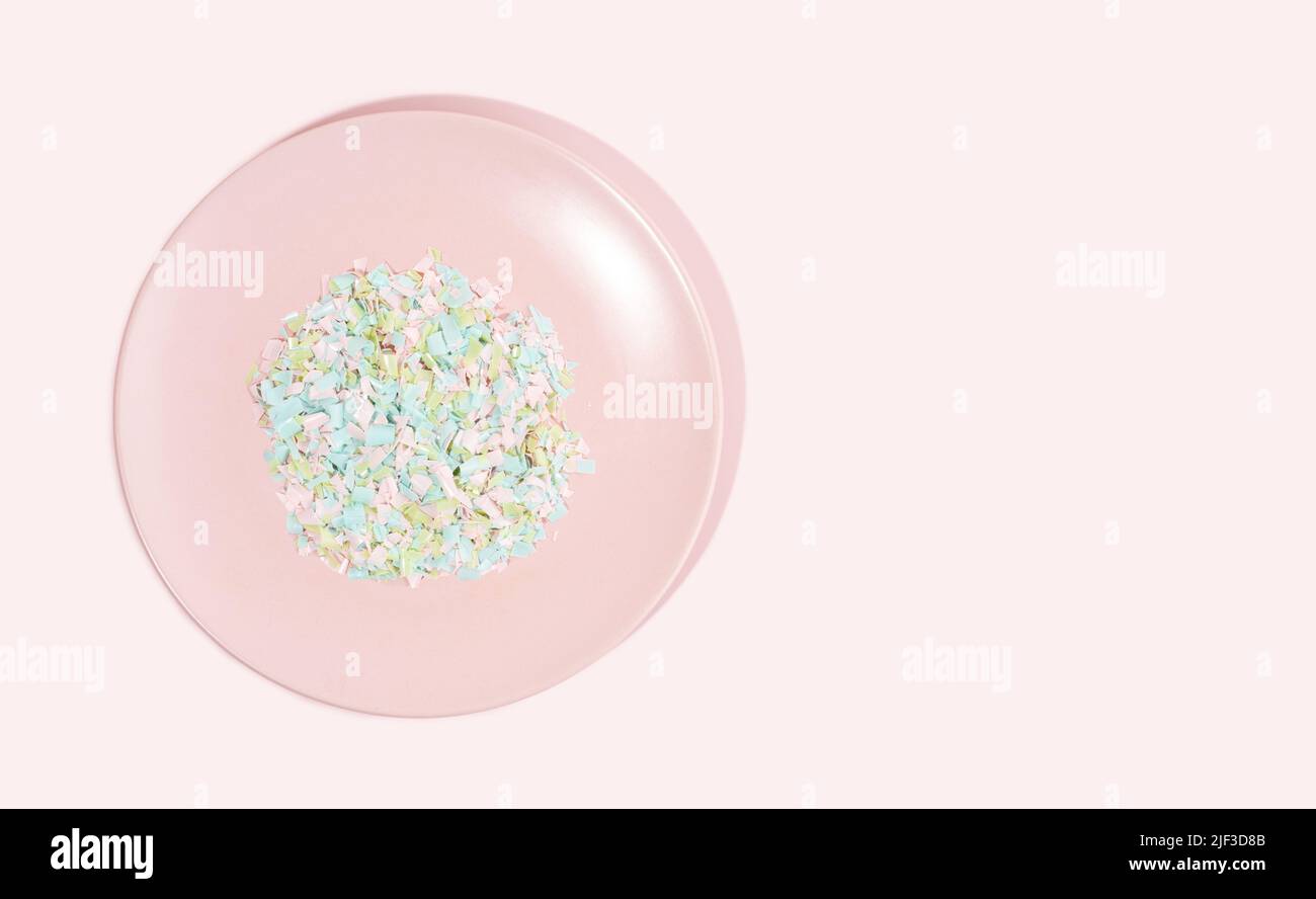 A plate full of microplastics on a pink background. Impact of micro plastic in food chain. The concept of plastic pollution. Composition of plate and Stock Photo