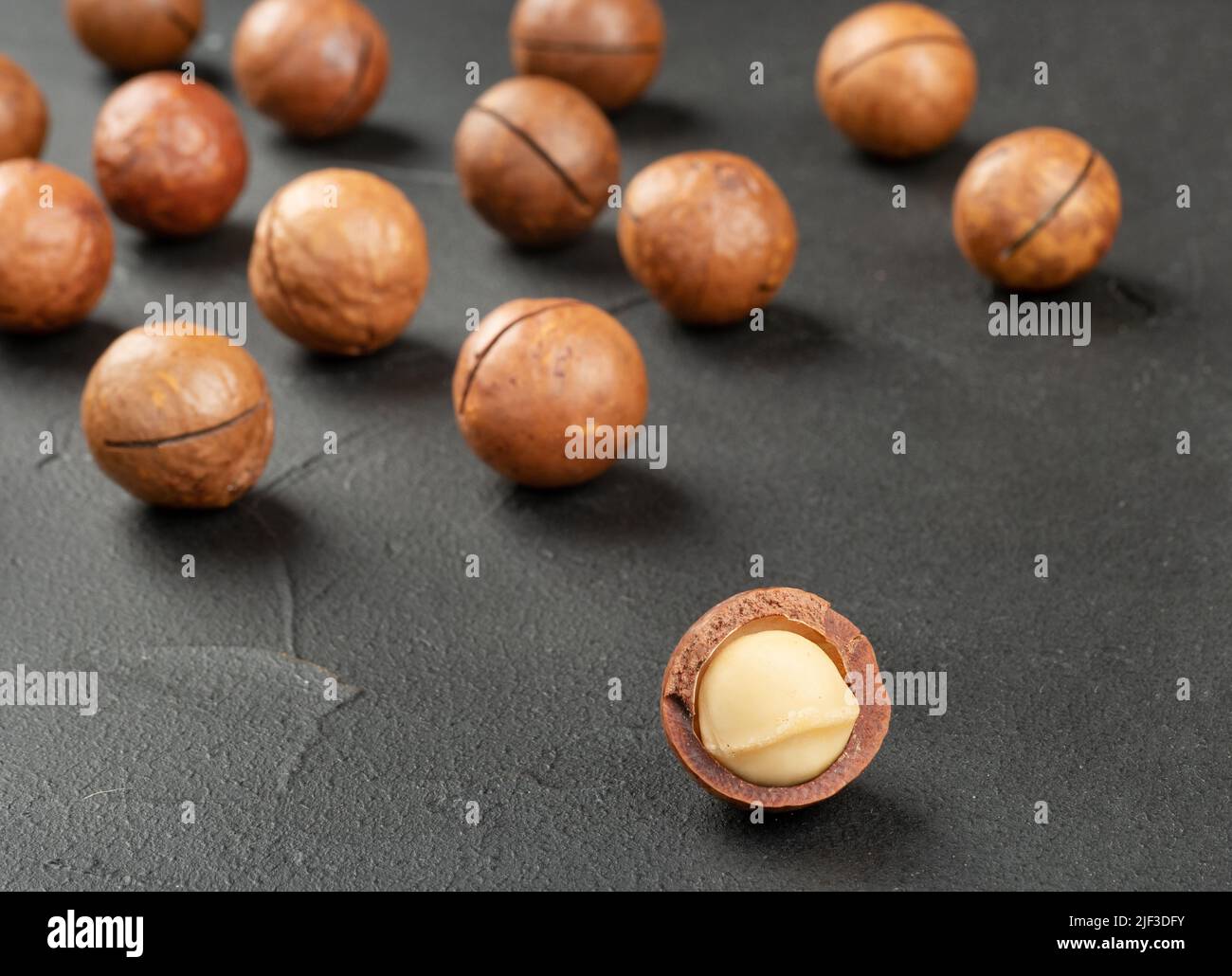 Scattered macadamia nuts in their shells on a dark concrete background Stock Photo