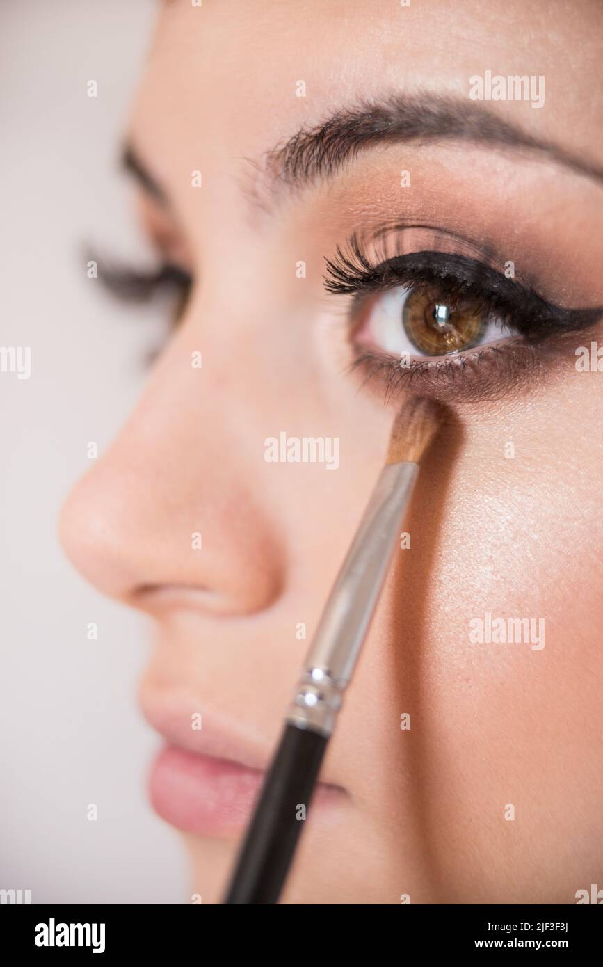 Macro detail of caucasian model brown almond eyes during make-up session. The make-up artist is applying a brown eye shadow with the brush.  The model Stock Photo
