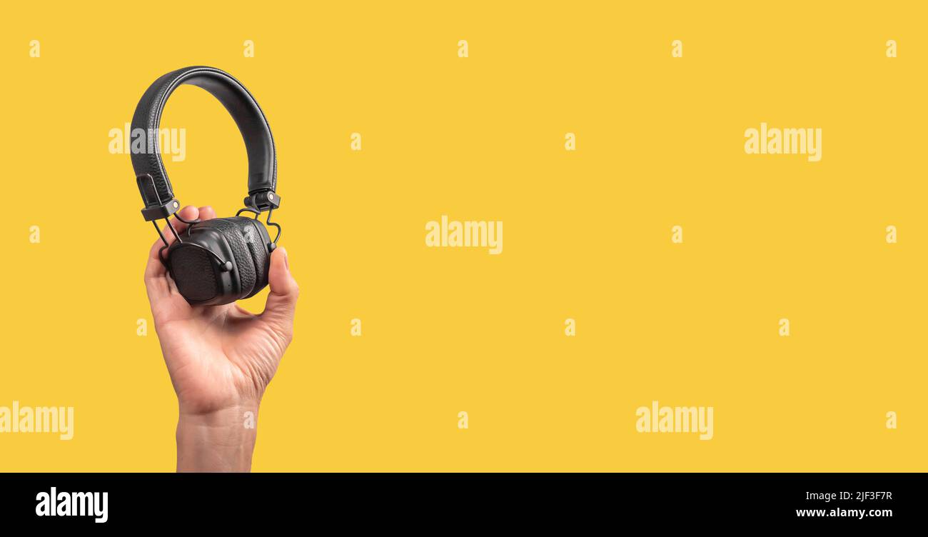 Banner with hand holding wireless headphones on yellow background. Listening to music, taking phone calls. Copy space. High quality photo Stock Photo