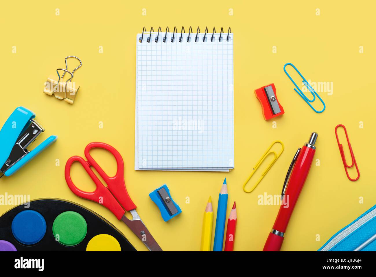 Top view of blank spiral notepad and school supplies with space for text on yellow background. Back to school concept Stock Photo