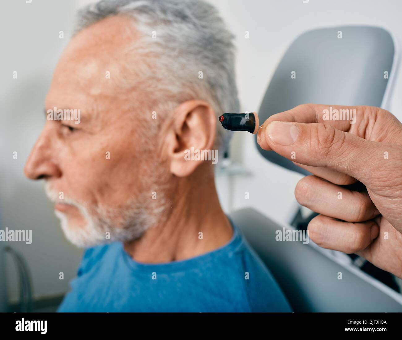 Closeup of intraear hearing aid, near senior male patient's ear at