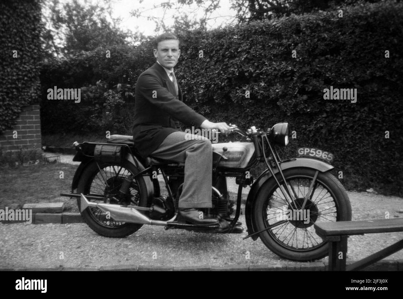 1930s, historical, a gentleman in a jacket & tie sitting in a driveway on a 'Douglas' motorcycle of the era, Newbury, Berks, England, UK. Douglas was a British motorcycle manufacturer based in Kingswood, Bristol, who operated from 1907 through to 1957. Owned by the Douglas family up to 1931, when it became a public company, they were known for their horizontally opposed twin cyclinder engined bikes and in the 1920s were awarded a prestigious royal warrant as Motor Cycle Manufacturers by Appointment to H. M. The King (King George VI). Stock Photo