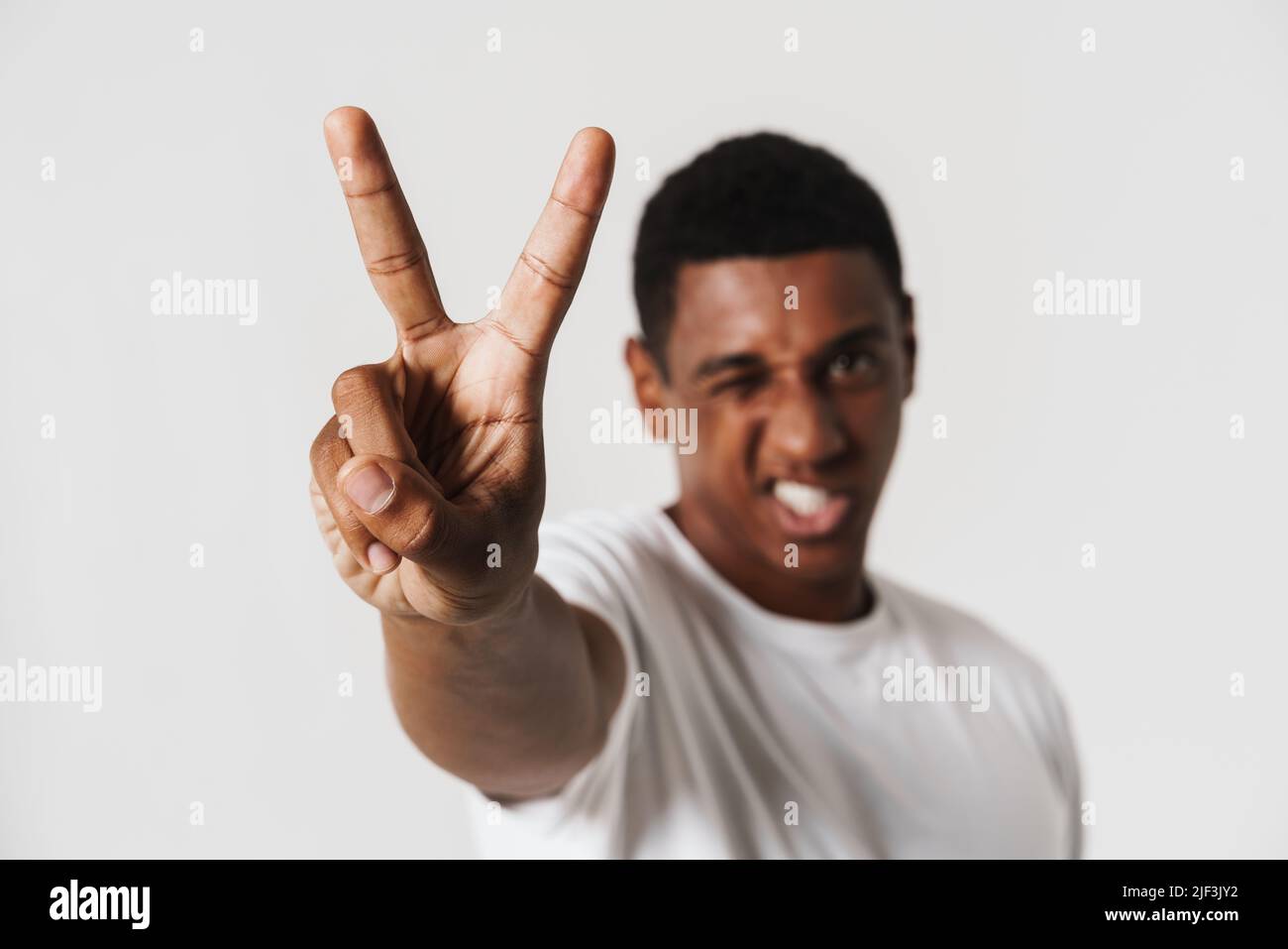 Young black man grimacing while showing peace sign isolated over white wall Stock Photo