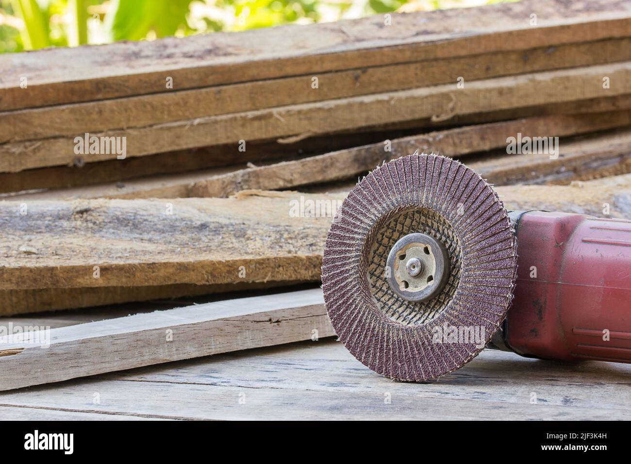 Electric sandpaper tool on wooden table with a pile of wood behind