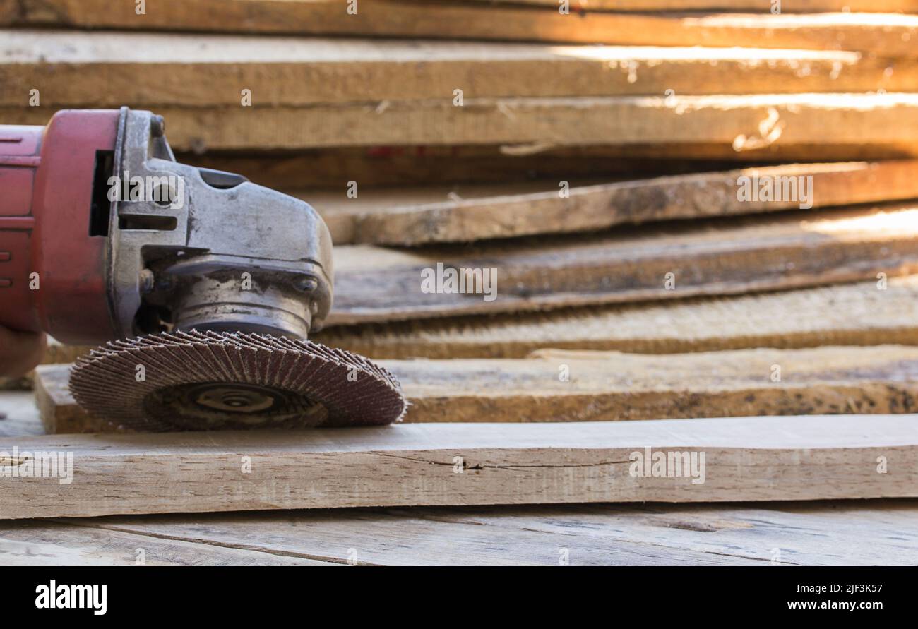 Electric sandpaper tool on wooden table with a pile of wood behind