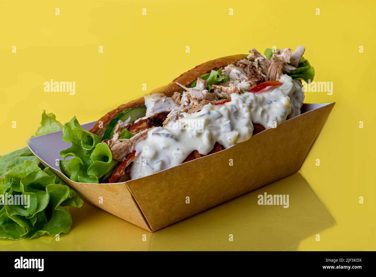 Hot dog with sausage in a paper box with tomatoes and corn, chili peppers, cucumber and lettuce. On a red background. Fast food. copy space Stock Photo