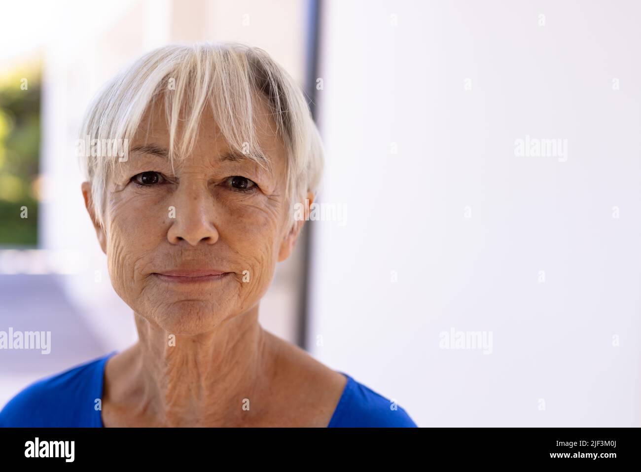 Close-up portrait of smiling asian senior woman with short hair against white wall in nursing home Stock Photo