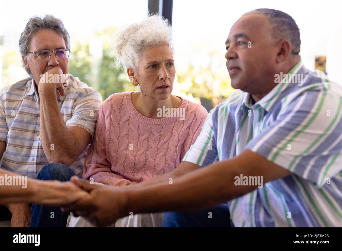 Multiracial seniors looking at man holding woman's hands and comforting her in group therapy session Stock Photo