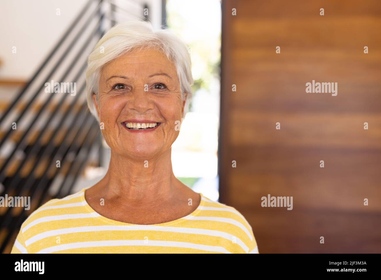 Close-up portrait of smiling biracial senior woman with short hair against door in nursing home Stock Photo