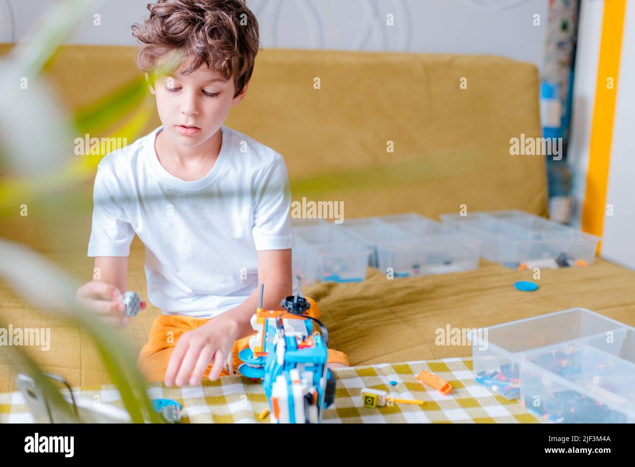 Kid collects robot from plastics details and programmed on tablet, robotics. Stock Photo