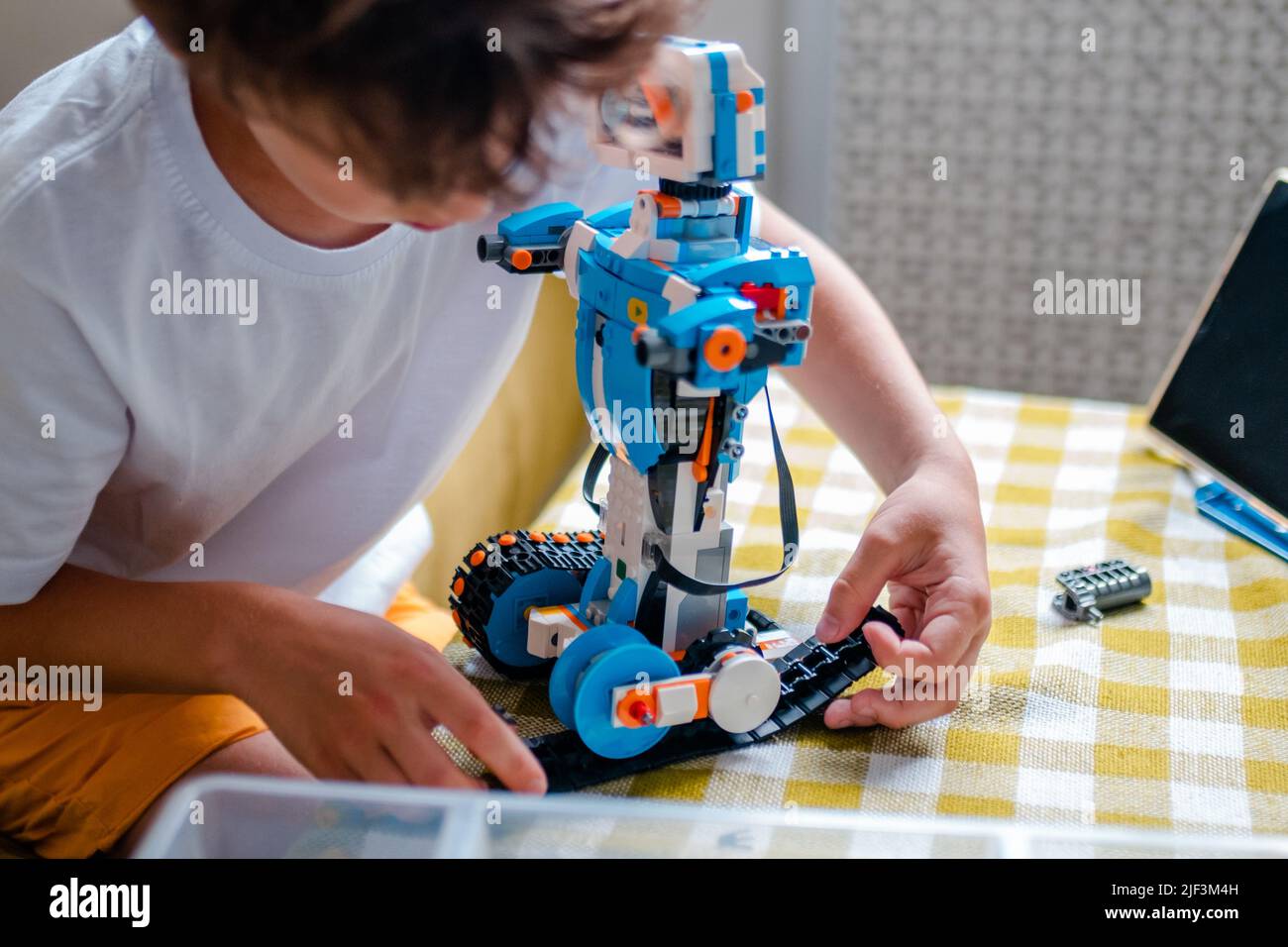 Kid collects robot from plastics details and programmed on tablet, robotics. Stock Photo