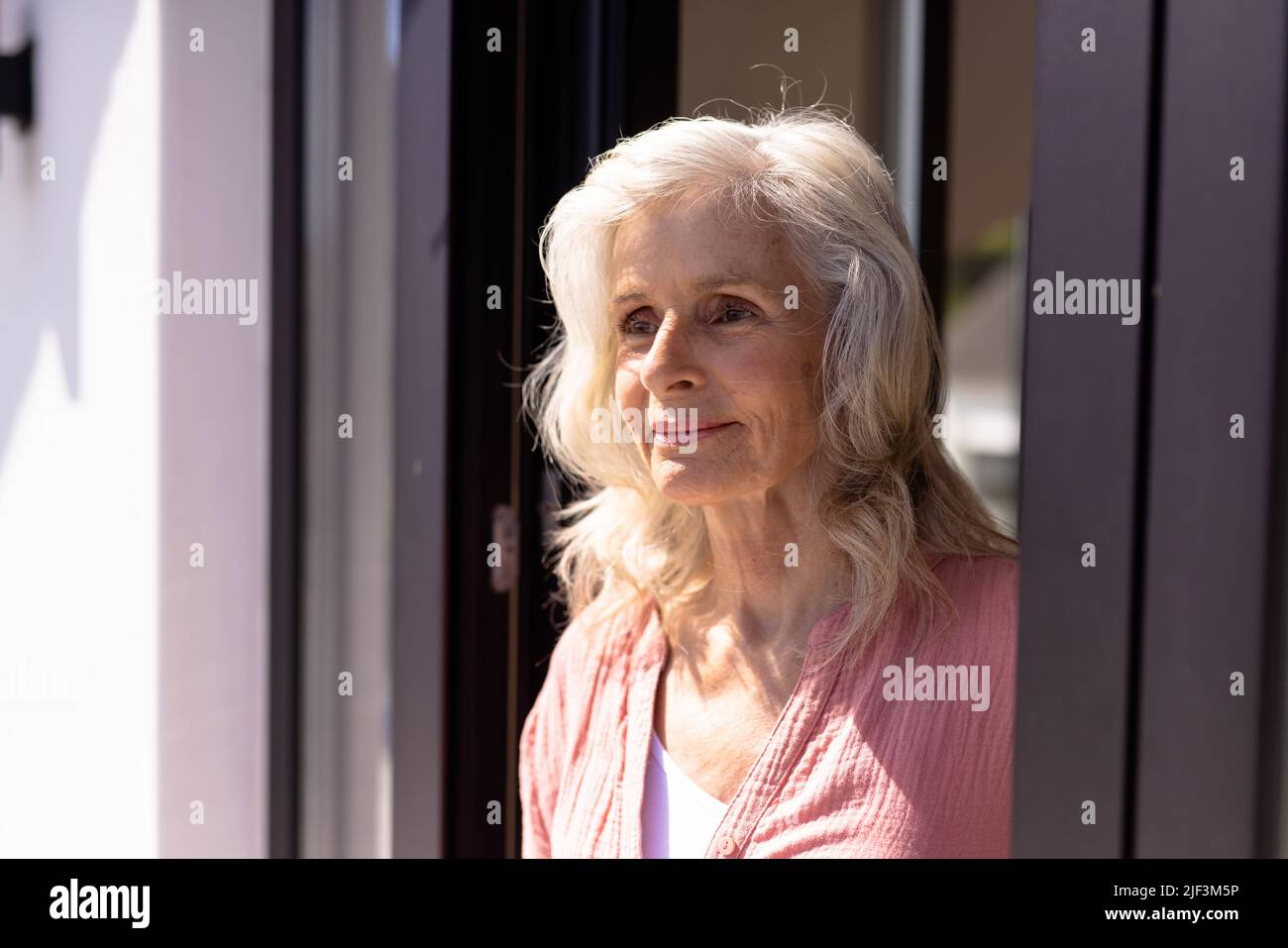 Caucasian thoughtful senior woman with wavy hair looking away by window at nursing home Stock Photo