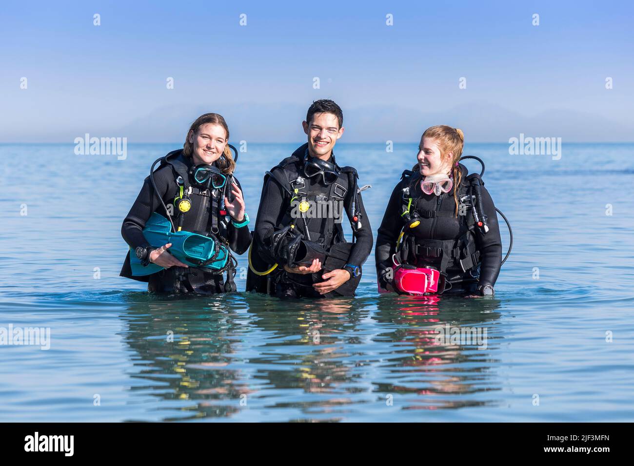 Scuba divers walking out of the sea after a shore dive happily talking to each other Stock Photo