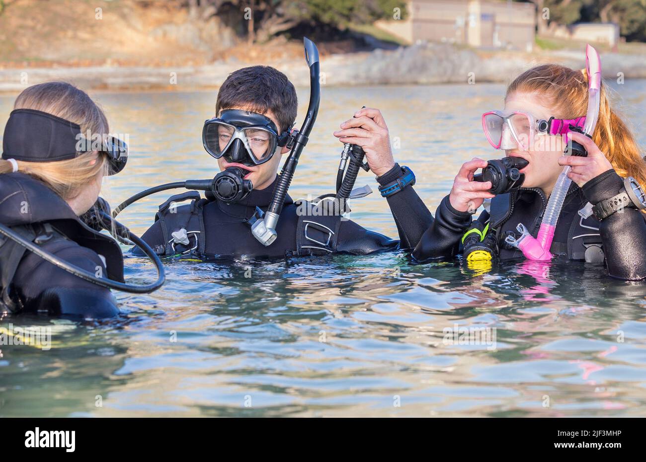 Scuba divers training in the sea looking at their instructor getting ready to submerge with their dive masks on and their deflator hoses lifted up Stock Photo