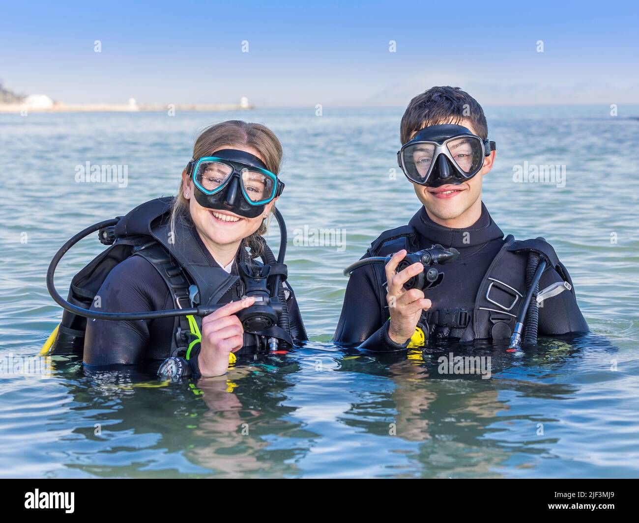 Smiling scuba divers in the sea, facing the camera with their dive masks on and their regulators in their hands Stock Photo
