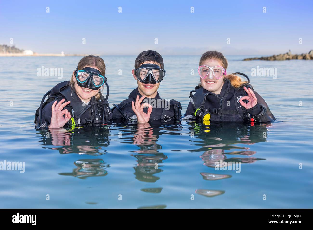 Smiling scuba divers in the sea, facing the camera with their dive masks on showing the OK sign Stock Photo