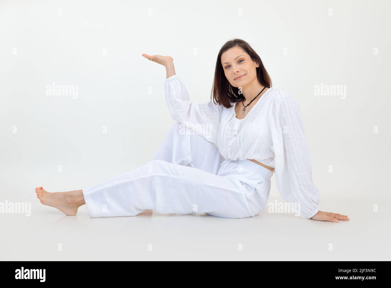Attractive smiling barefoot brown-haired woman in white outfit sit ...