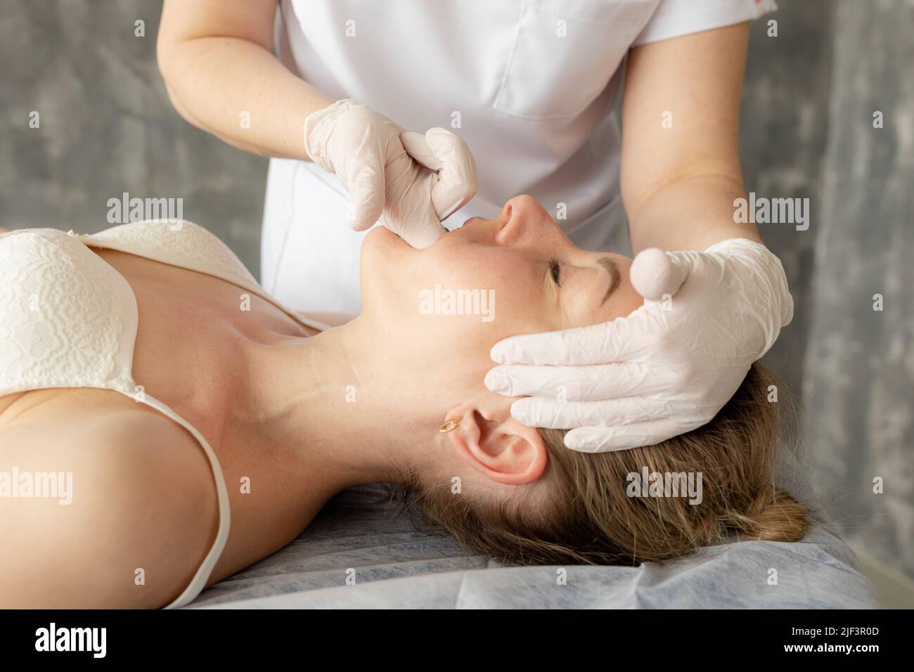 Female physiotherapist, chiropractor, osteopath doing anti wrinkle manual myofascial face massage by fingers in mouth Stock Photo